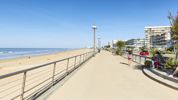 A coastal promenade with a beach, a pedestrian path, and residential buildings.