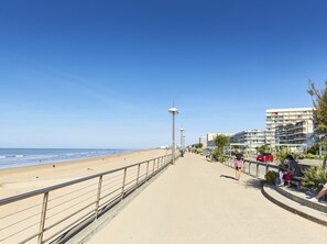 Une promenade en bord de mer, avec une plage, un chemin piétonnier et des immeubles d’habitation.