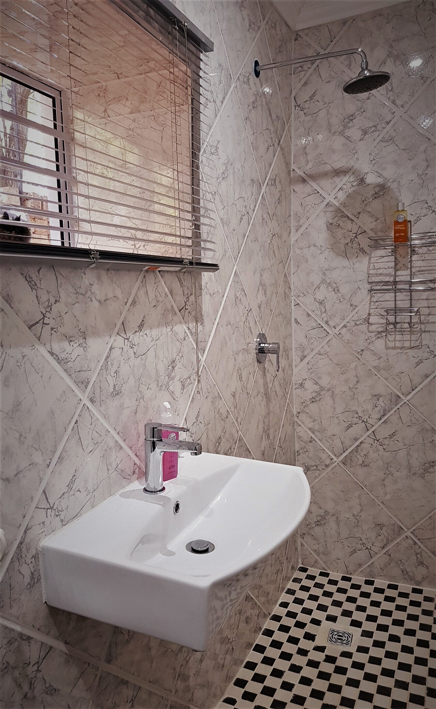 A bathroom with a white sink, a shower, and a window with blinds.