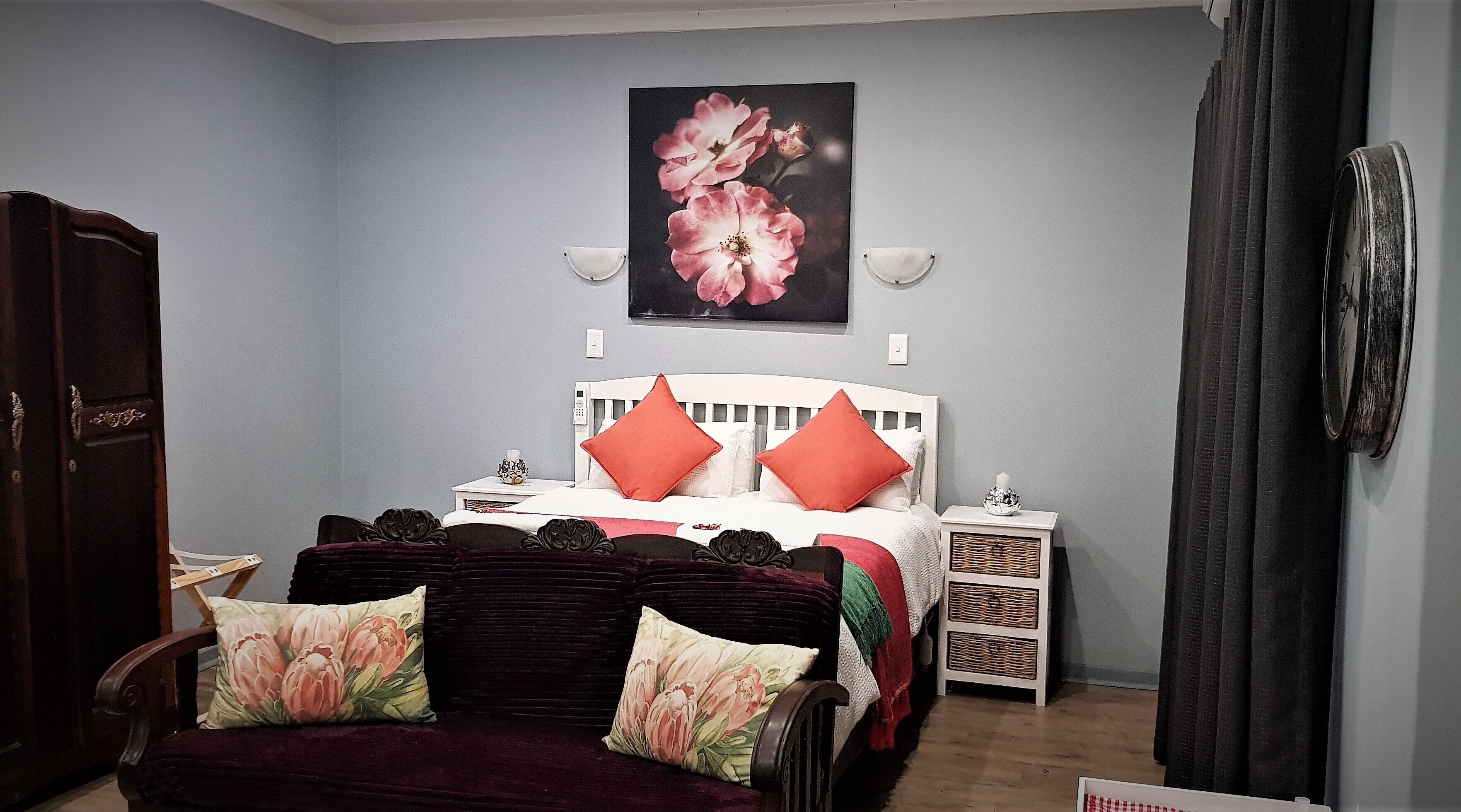 Un dormitorio con una cama, dos mesitas de noche, un aparador y un cuadro grande con motivos florales en la pared.