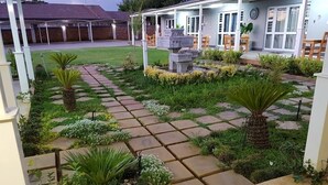 A well-maintained garden with stone pathways, various plants, and a covered seating area with chairs. - Graceland Guest House (Potchefstroom)
