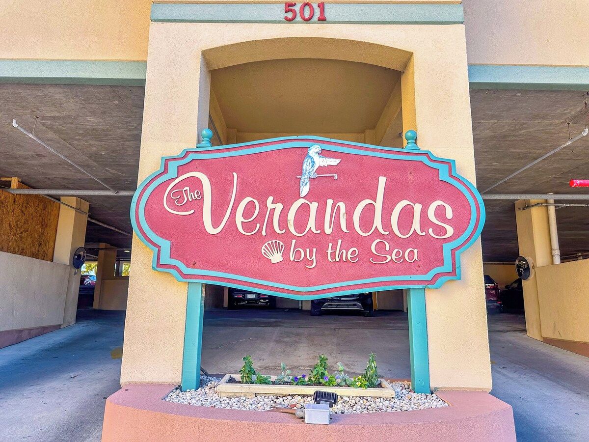 A sign for 'The Verandas by the Sea' with a bird illustration, located under a covered parking area.