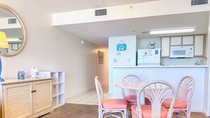 A compact room with a kitchenette, a dining area with wicker chairs, and a small cabinet.