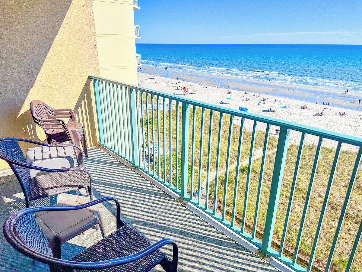 A balcony with a view of a beach, equipped with chairs and a railing.