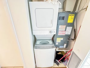 Une petite buanderie équipée d’un lave-linge et d’un sèche-linge à chargement frontal, d’un panneau de commande avec des consignes de sécurité et d’une tuyauterie visible.
