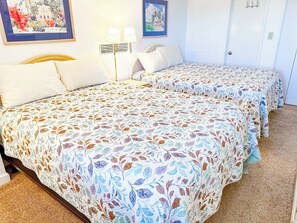 Une chambre d'hôtel avec deux lits, chacun recouvert d'une couvre-lit à motifs floraux, une lampe de chevet et un tableau encadré au mur.