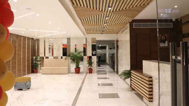 A modern lobby with a wooden ceiling, marble flooring, and potted plants. - Hotel Le Amor (Kota)