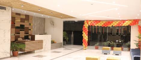 A modern reception area with a checkered wooden wall, a marble reception desk, and a colorful balloon arch. There are potted plants and a blue sofa in the space.