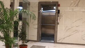 An elevator in a lobby with marble walls and potted plants. - Hotel Le Amor (Kota)