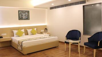 A modern hotel room with a large bed, two chairs, a bedside table, and a painting on the wall.
