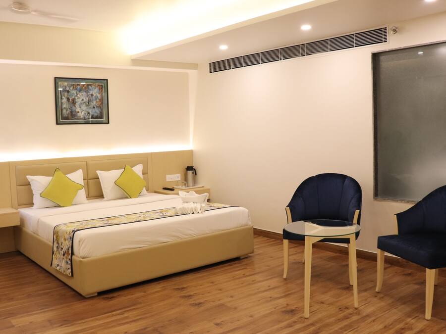 A modern hotel room with a large bed, two chairs, a bedside table, and a painting on the wall.