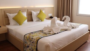 A hotel room with a large bed, floral bedspread, and a swan towel arrangement. - Hotel Le Amor (Kota)