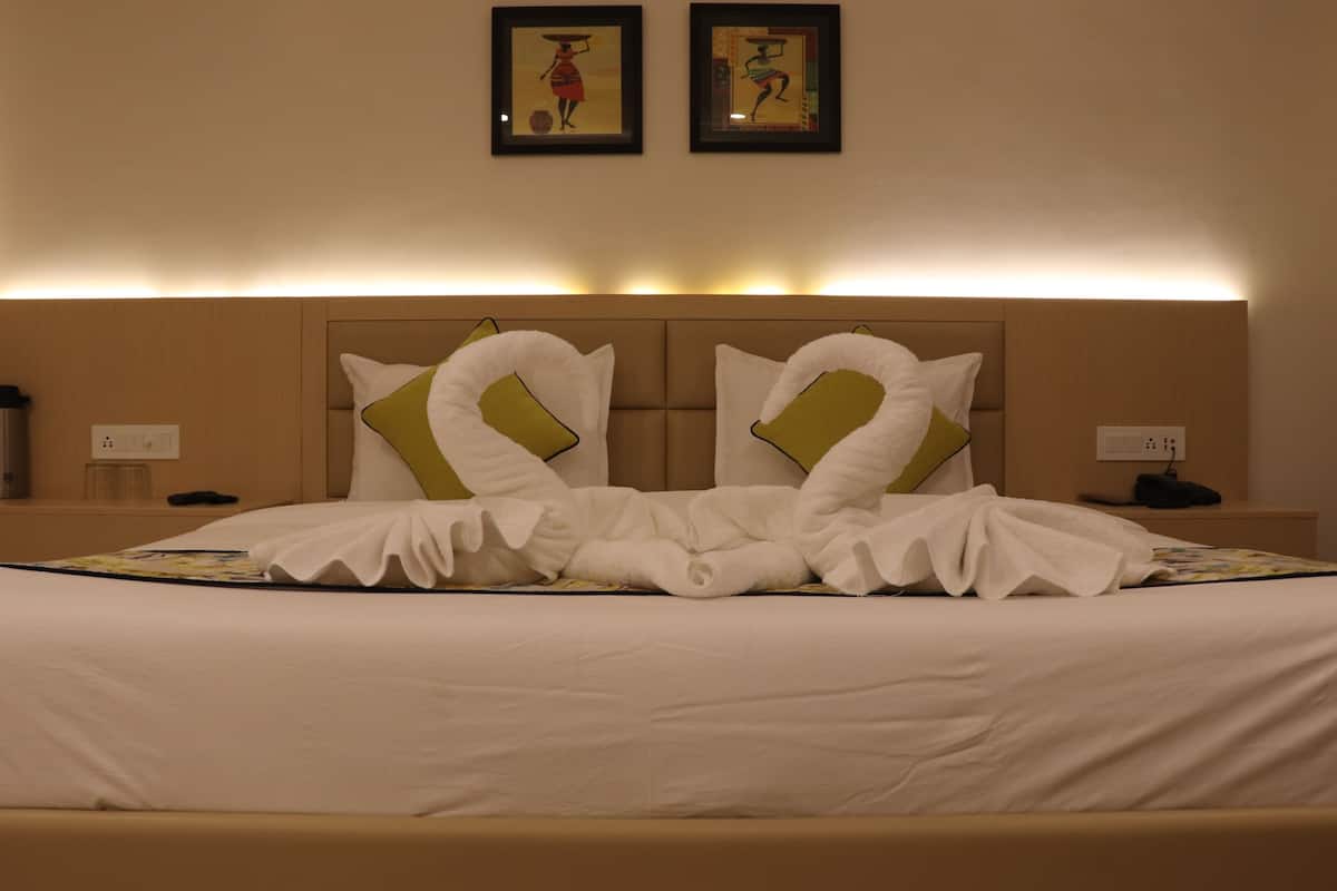 A neatly made bed with a headboard, two framed pictures on the wall above, and a bedside table with a lamp and phone.