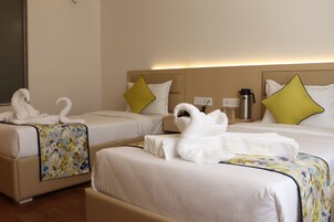 Habitación de hotel con dos camas, cada una con una colcha estampada y una toalla blanca doblada en forma de cisne. En cada cama hay dos almohadas, una amarilla y otra blanca.