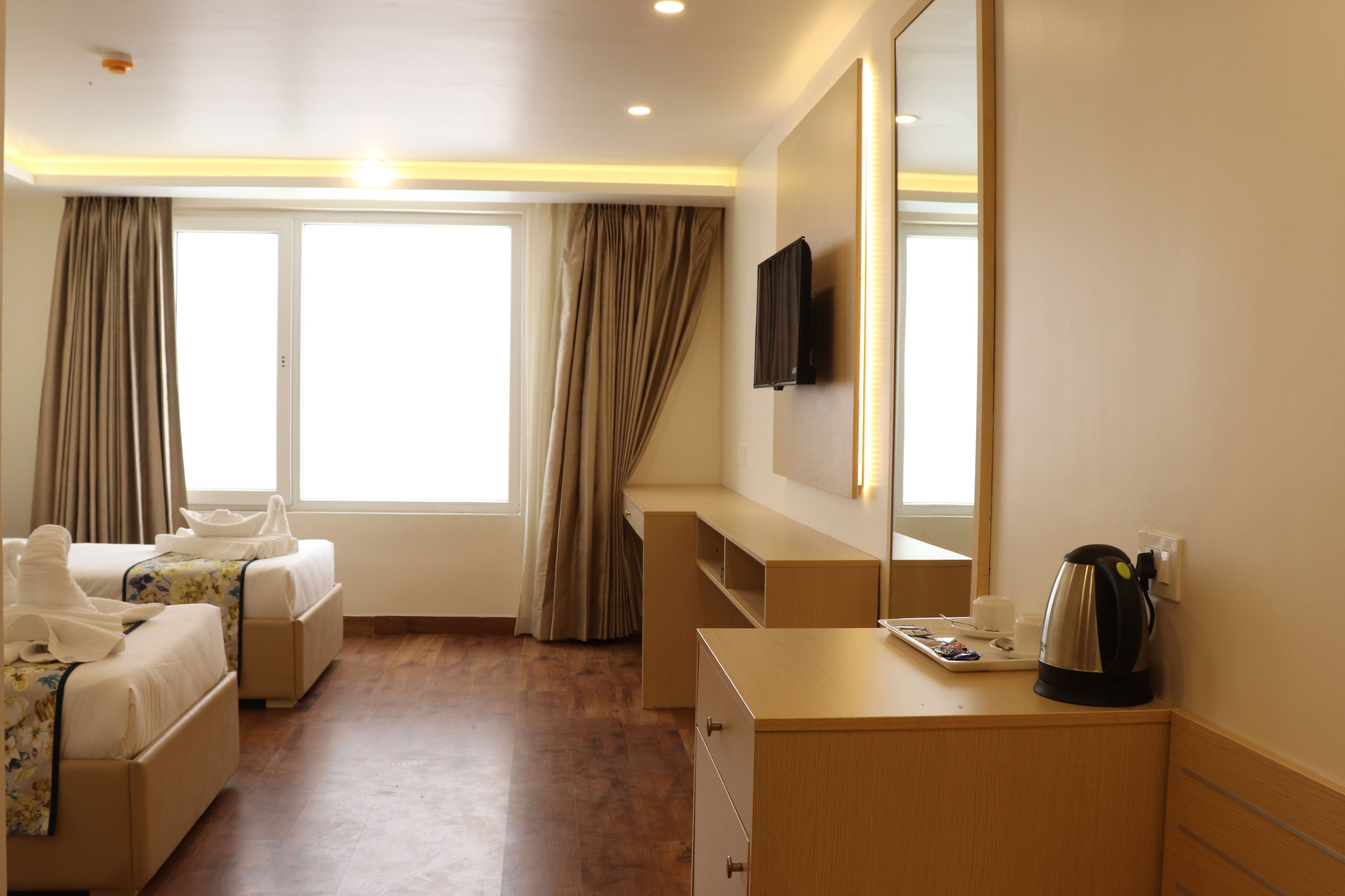 A hotel room with two beds, a desk, a mirror, a television, and a coffee maker.