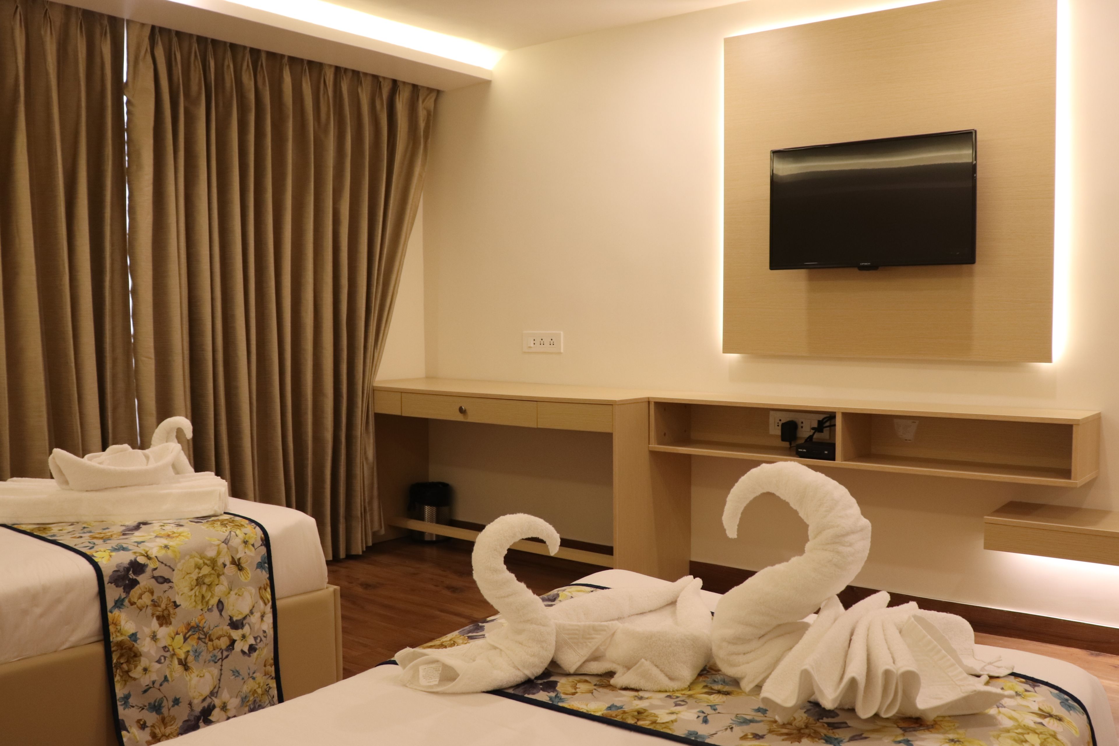 A hotel room with two beds, a TV mounted on the wall, and a desk with a chair.