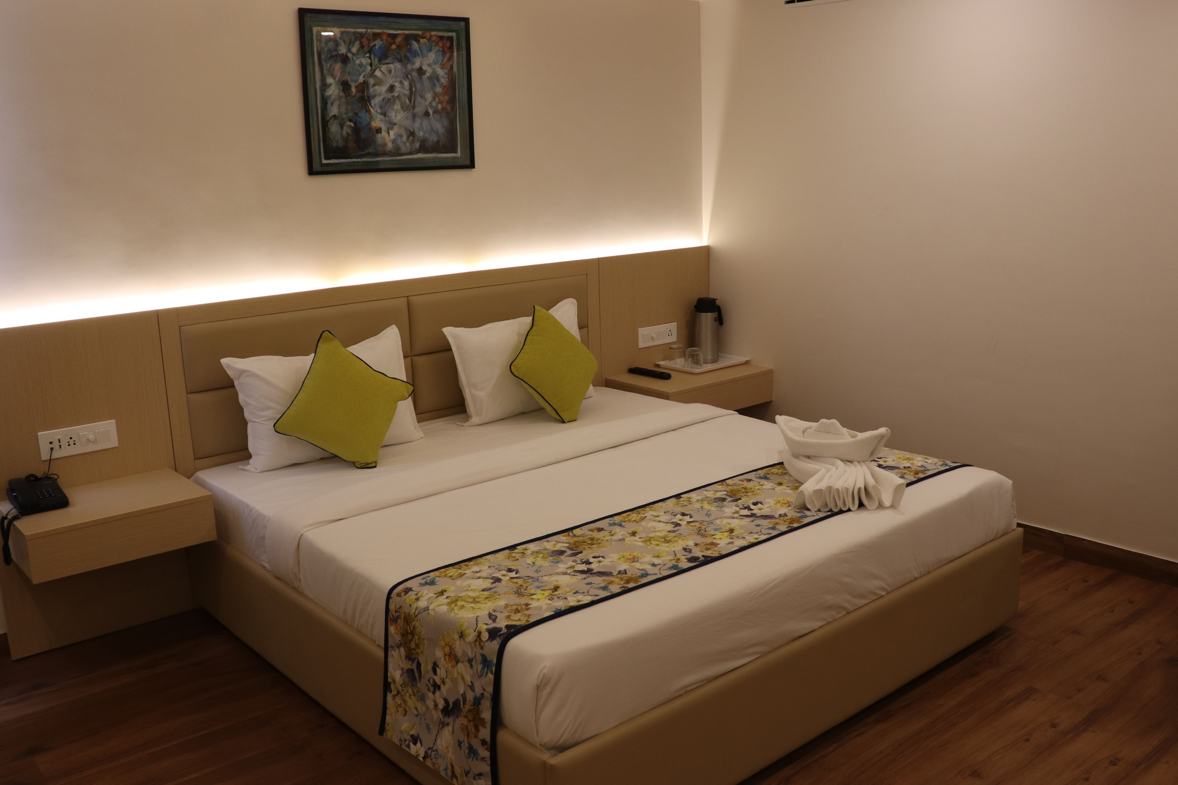 Uma cama bem arrumada com colcha floral, uma mesa de cabeceira com telefone e abajur, e um quadro na parede.