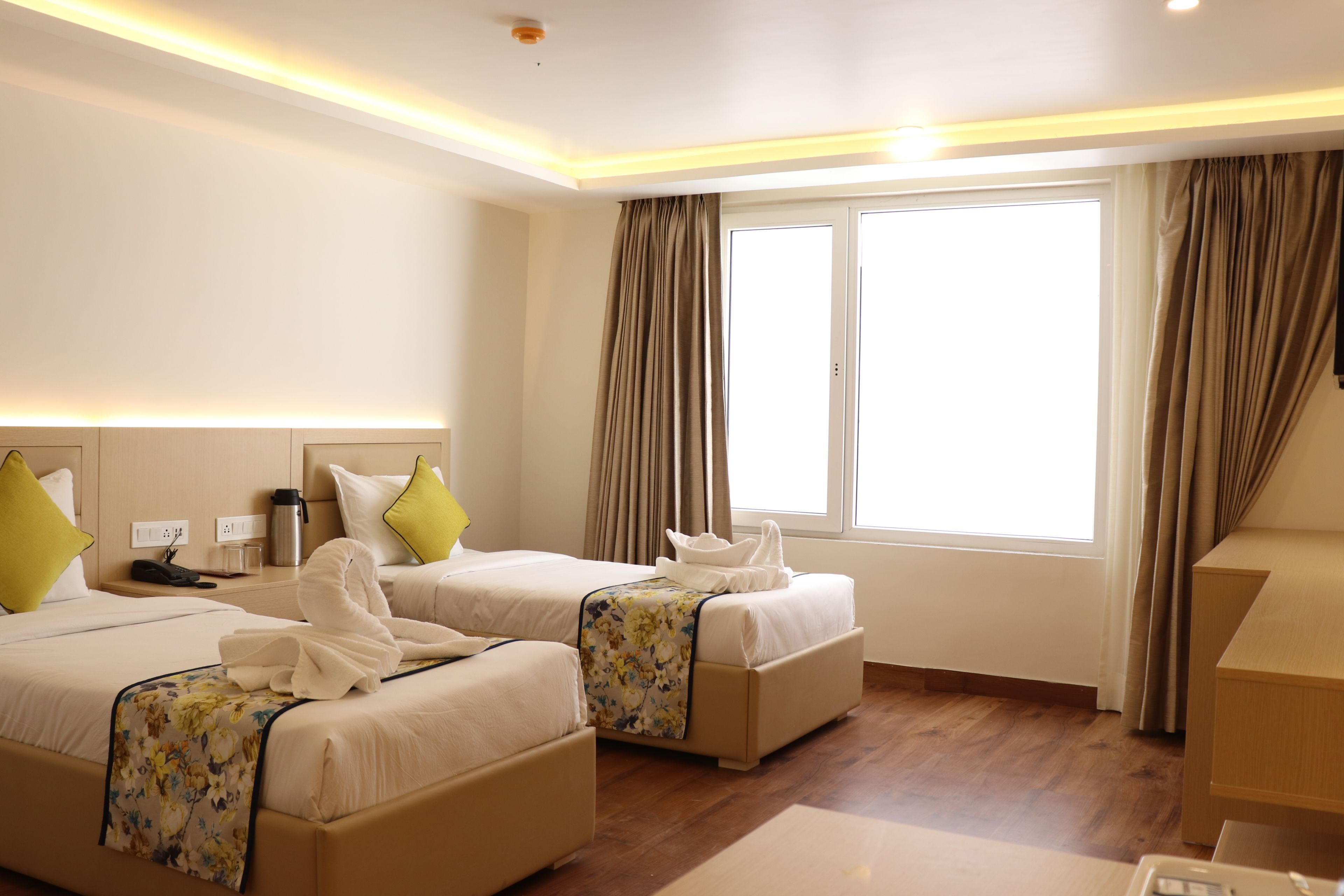 A hotel room with two beds, a desk, a chair, and a window with curtains.