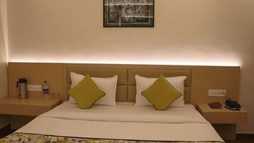 Une chambre d’hôtel avec un lit, deux tables de chevet, un tableau encadré et une petite table de nuit avec un téléphone et un livre.