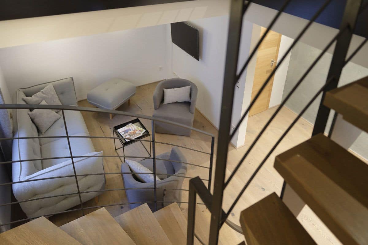 A modern interior with a staircase, grey sofas, a small table, and a mounted TV.