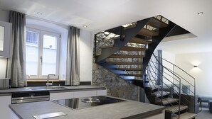 A modern kitchen with a central island, a built-in stove, and a stone accent wall. - Haus Heimat 1883 (Garmisch-Partenkirchen)