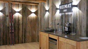 A rustic kitchen with wooden walls, a wooden countertop, a sink, a kettle, and skis leaning against the wall. - Haus Heimat 1883 (Garmisch-Partenkirchen)
