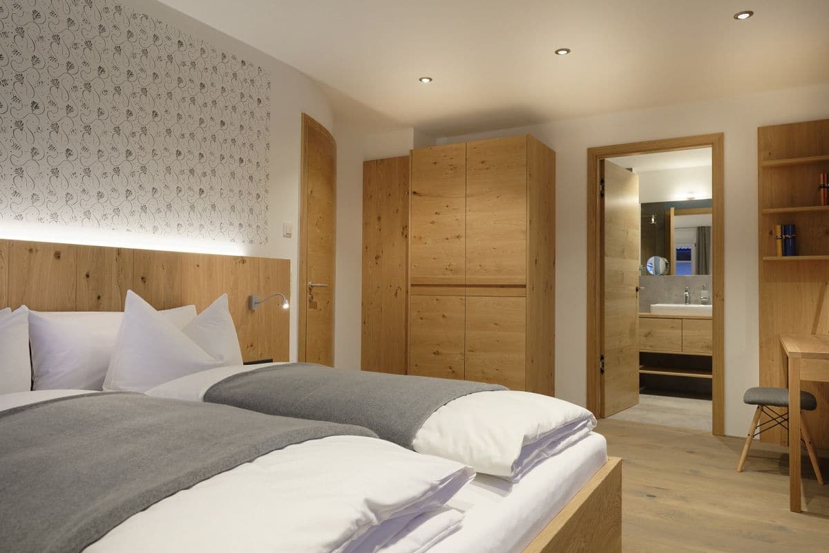 A modern bedroom with a large bed, wooden wardrobe, and a small desk with a chair.
