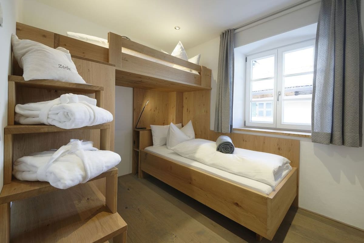 A bunk bed room with wooden shelves holding towels and pillows.