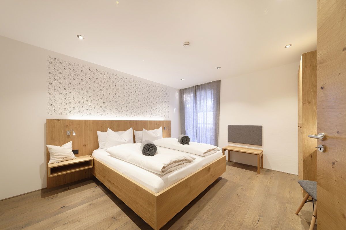 A modern bedroom with a large bed, bedside tables, a bench, and a TV.