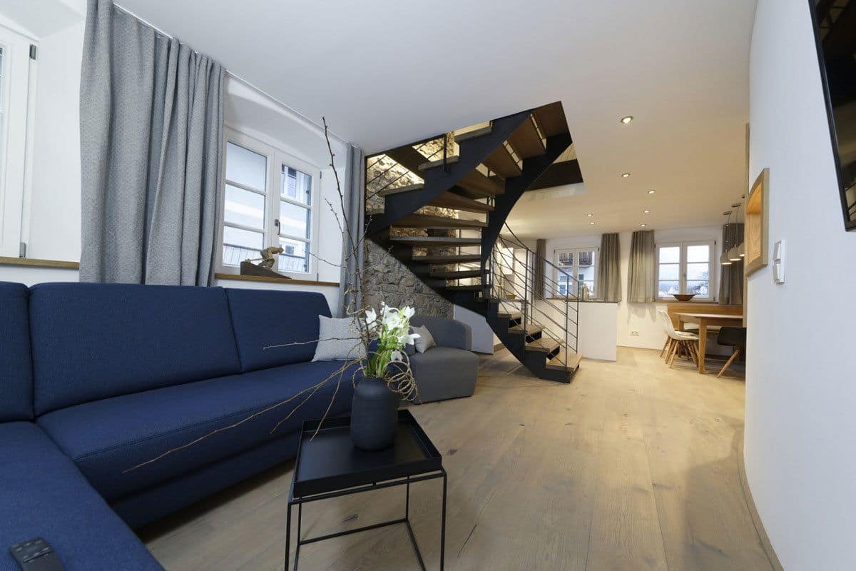 A modern living room with a blue sofa, a black coffee table, and a unique black spiral staircase.