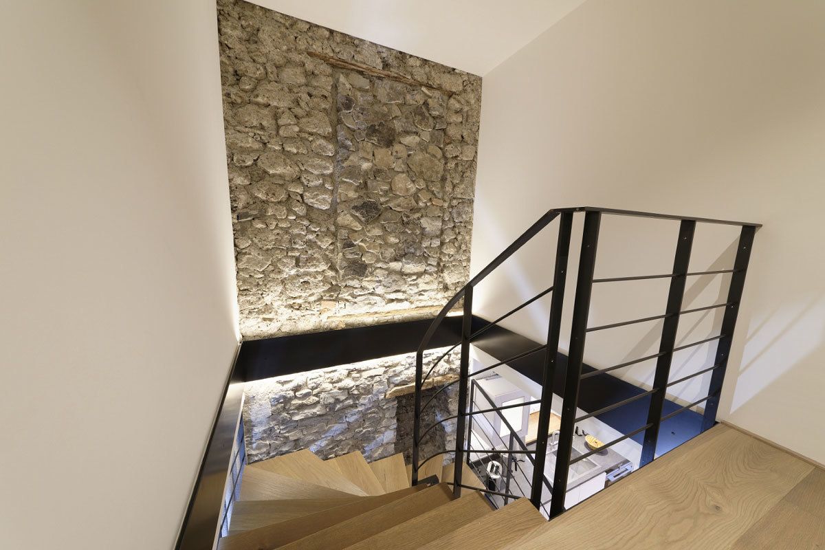 A staircase with a stone wall, black metal railing, and wooden steps.