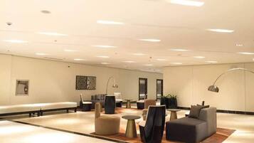 Um hall amplo com design moderno, apresentando uma área de estar com sofás e poltronas, uma mesa de centro e uma grande obra de arte na parede.