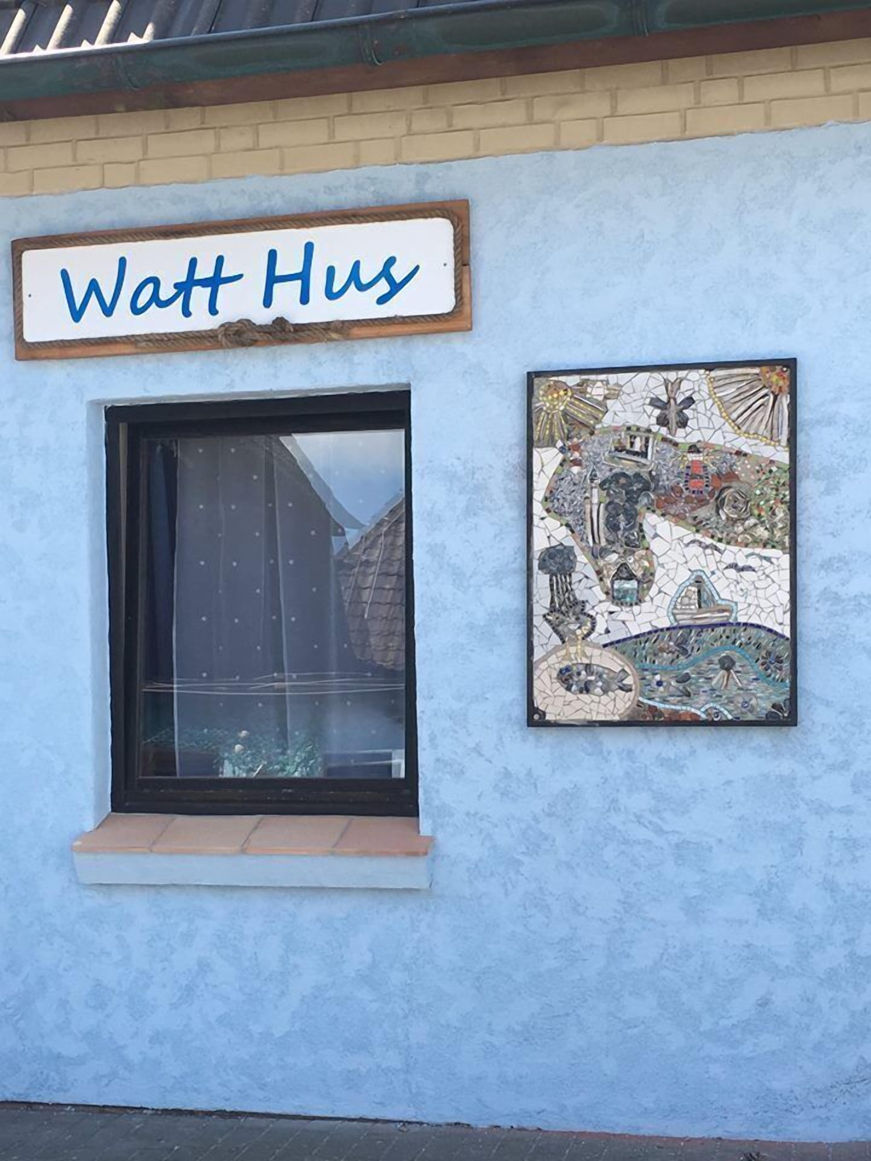A building with a sign reading "Watt Hus" and a mosaic artwork on the wall.