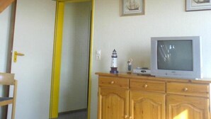 Una habitación con una escalera de madera, un televisor sobre un mueble de madera y una puerta con un listón amarillo.