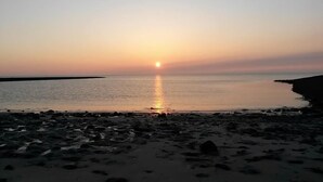 Una playa al atardecer con agua tranquila que refleja el cielo.