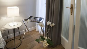 A hotel room with a wooden floor, a white lamp, a small table, a magazine, and a door with a frosted glass panel. - Hotel Il Sole (Empoli)