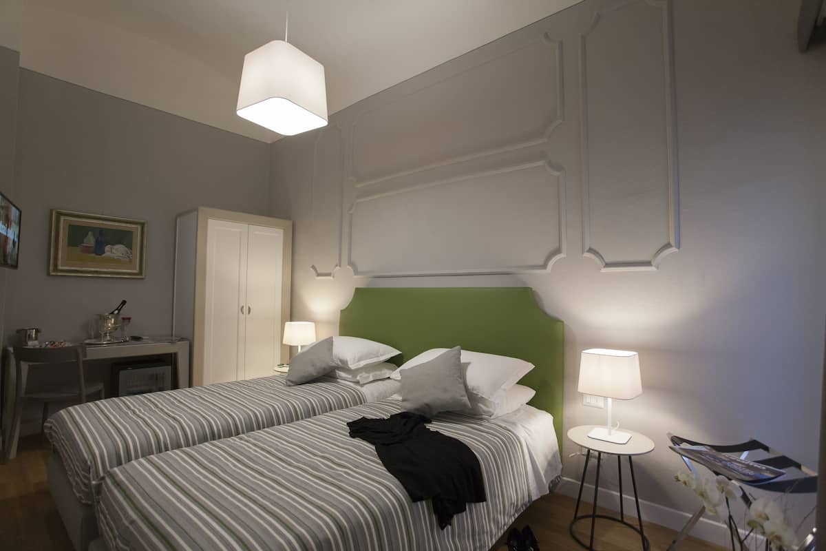 A hotel room with two beds, a desk, a chair, a wardrobe, and a lamp.
