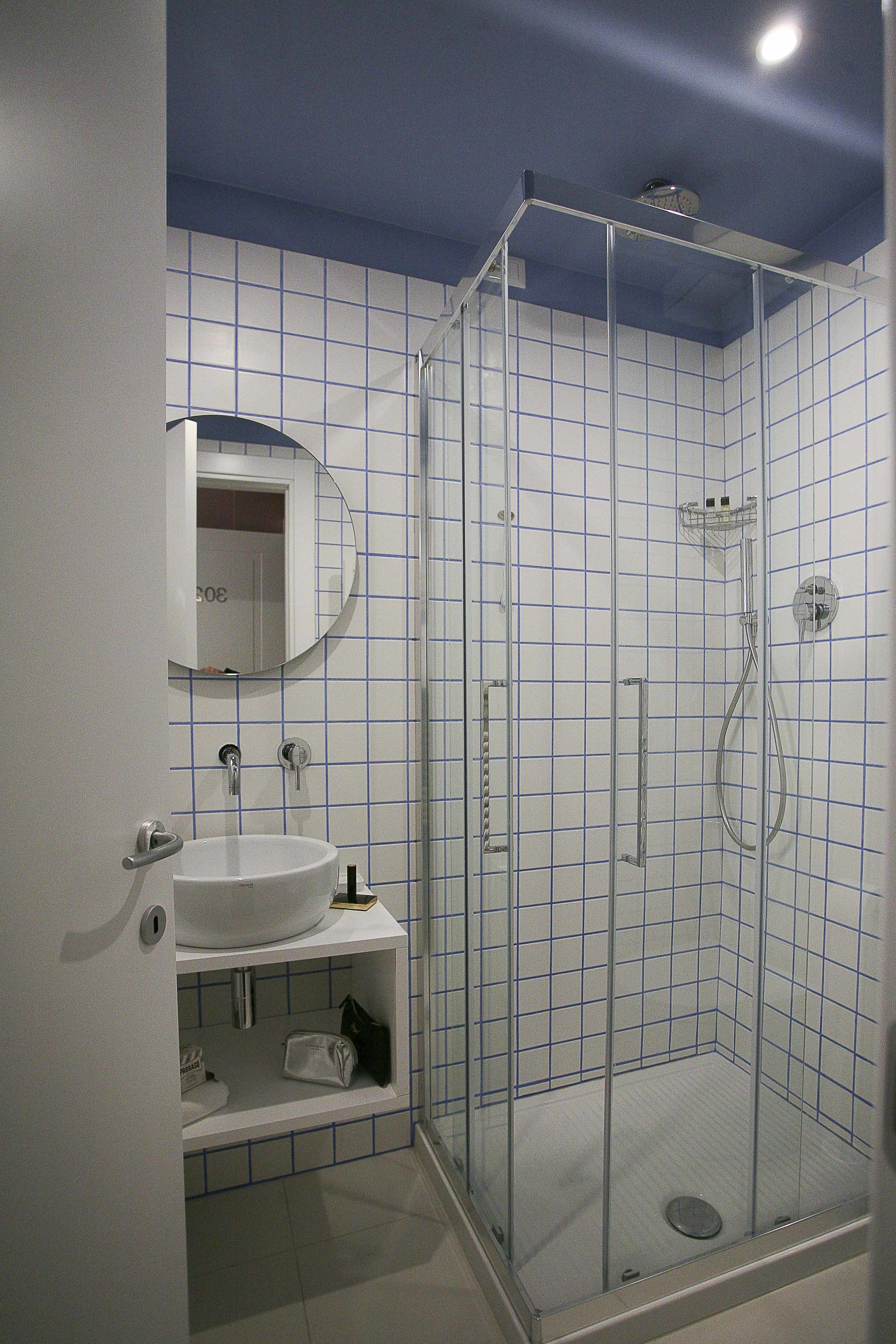 Ett modernt badrum med en dusch som är avskärmad med glasväggar, ett vitt handfat och en spegel ovanför.