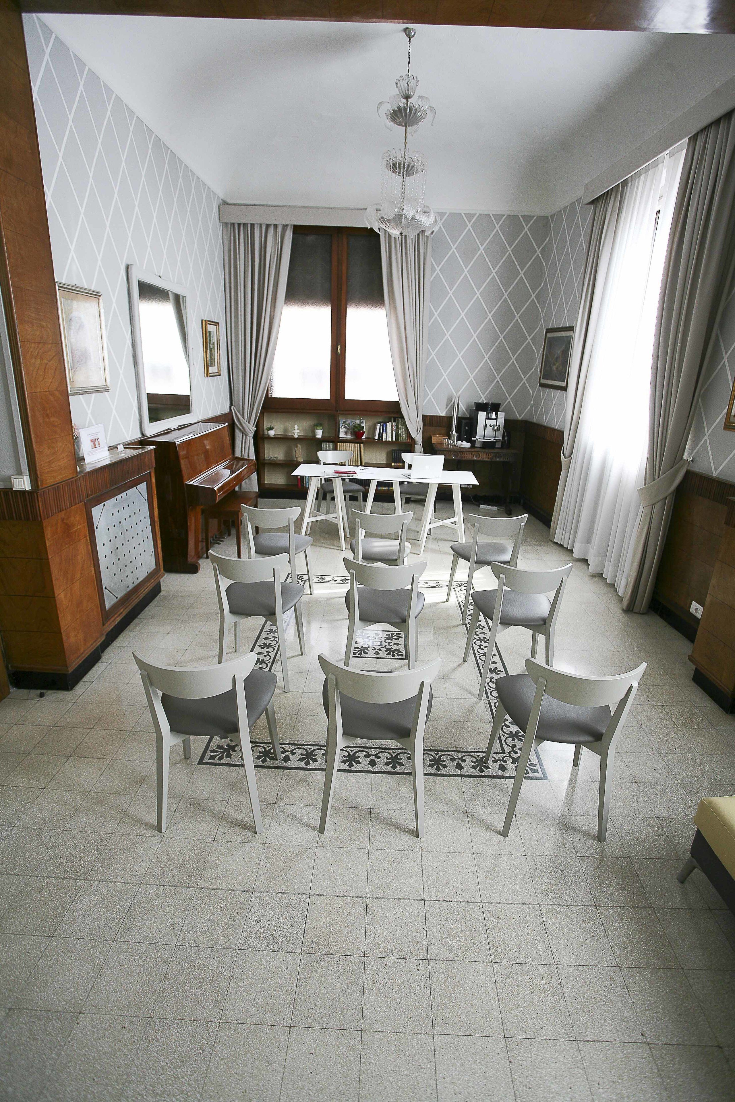 A dining area with white chairs, a piano, and a chandelier.