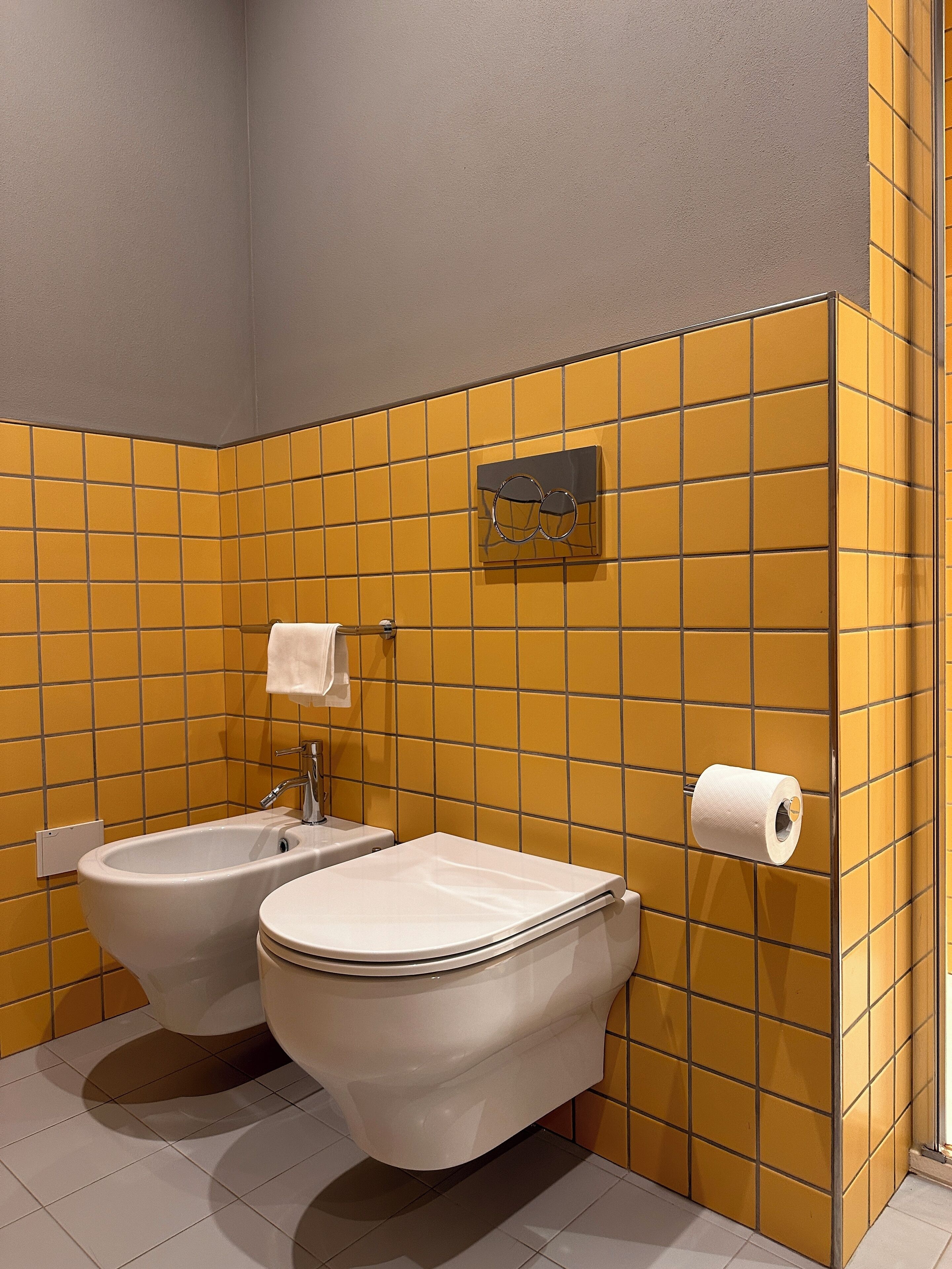 Un baño con paredes de azulejos amarillos, un bidé, un inodoro y un perchero para toallas.