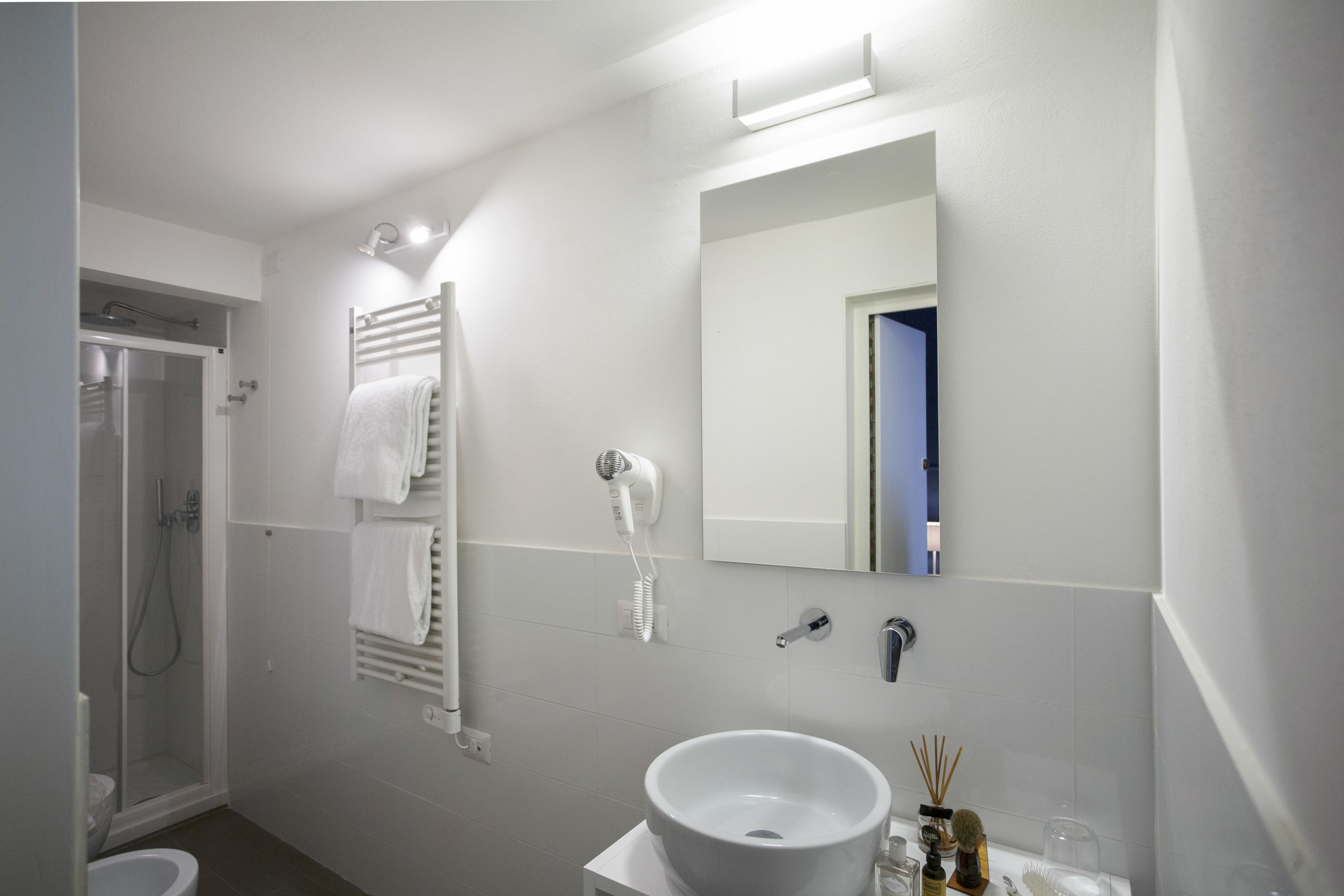 A modern bathroom with a white sink, a handheld hair dryer, a towel rack, and a shower.