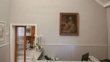 A reception area with a desk, a framed portrait on the wall, a staircase with ornate railings, and a patterned carpet.