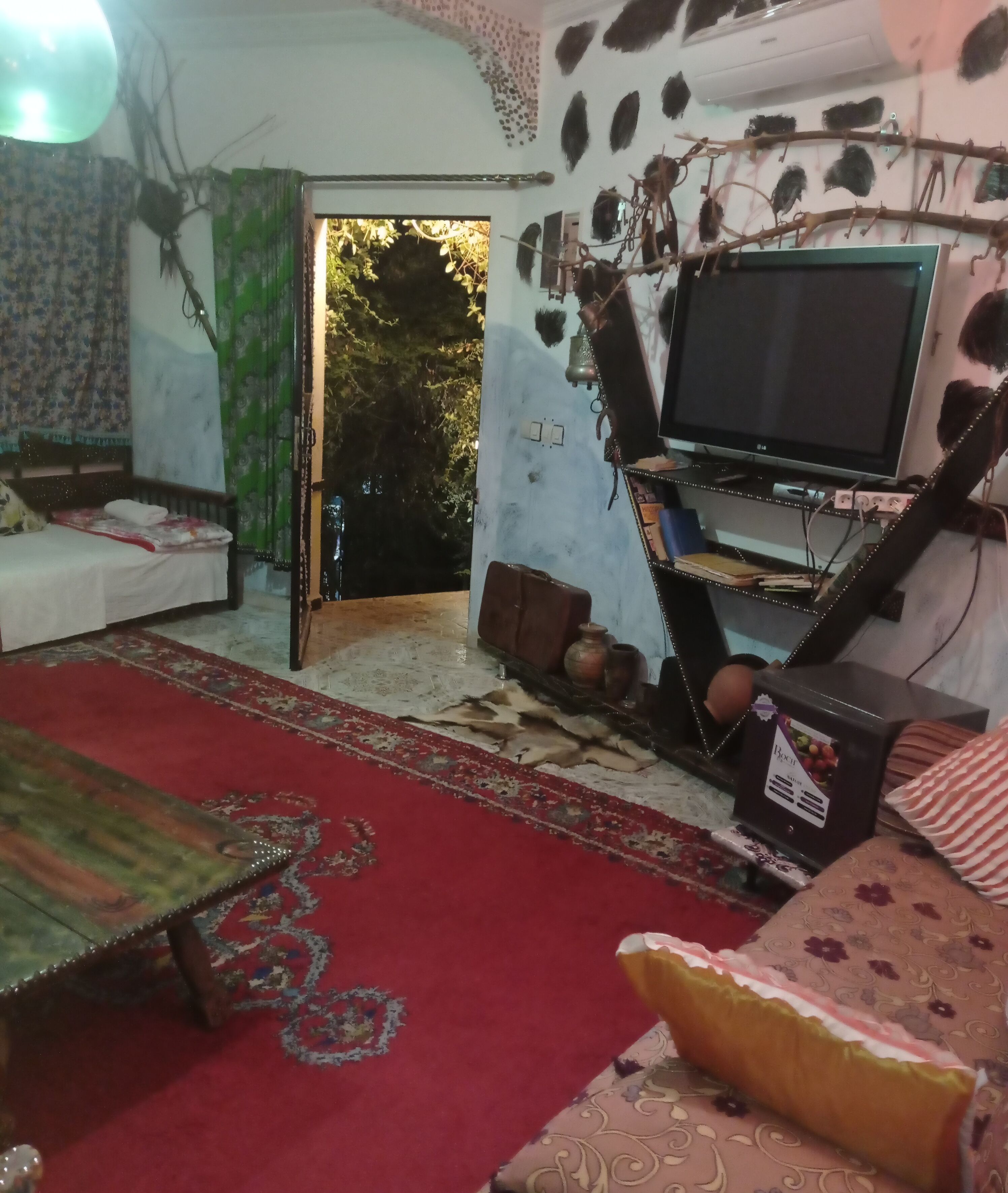 Uma sala de estar com televisão, tapete vermelho, sofá e tapete estampado.