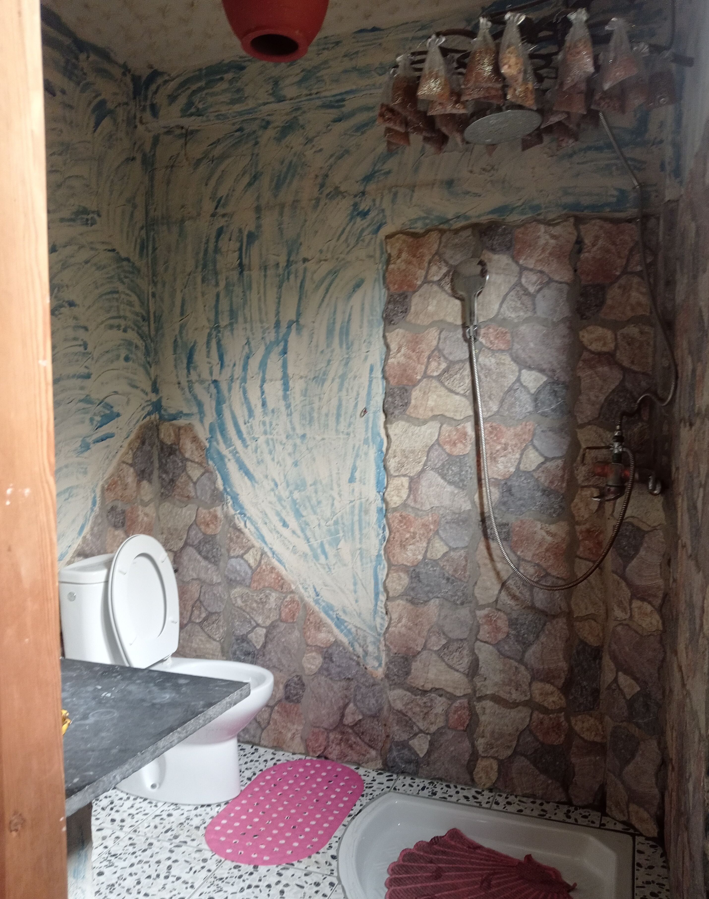 A bathroom with a stone shower wall, a white toilet, and a pink mat.