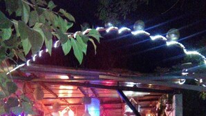 Een terras met tafels en stoelen, een overdekte zithoek en decoratieve verlichting.