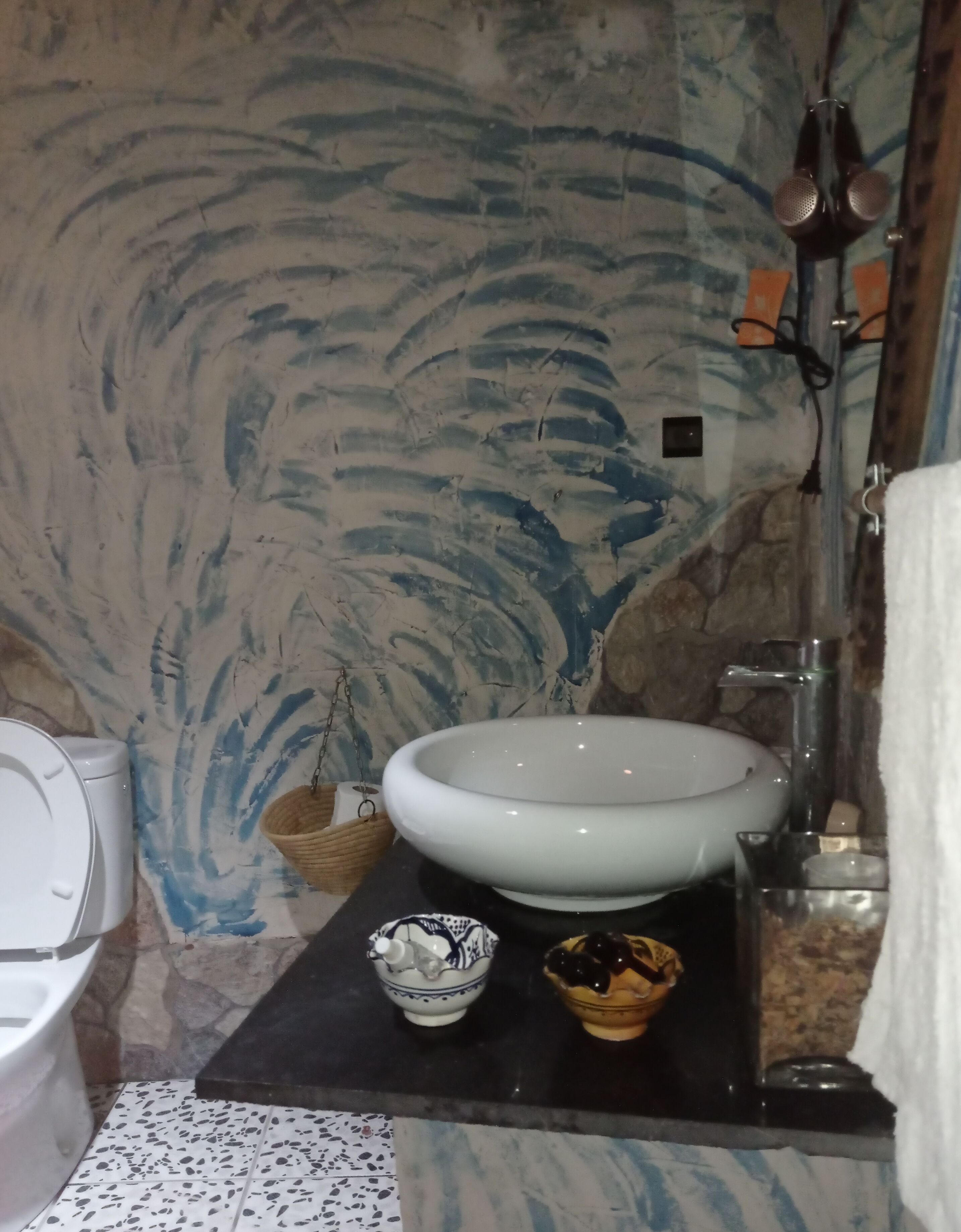 Une salle de bain avec des toilettes blanches, un grand lavabo blanc, un petit bol décoratif et une serviette suspendue à un porte-serviettes.
