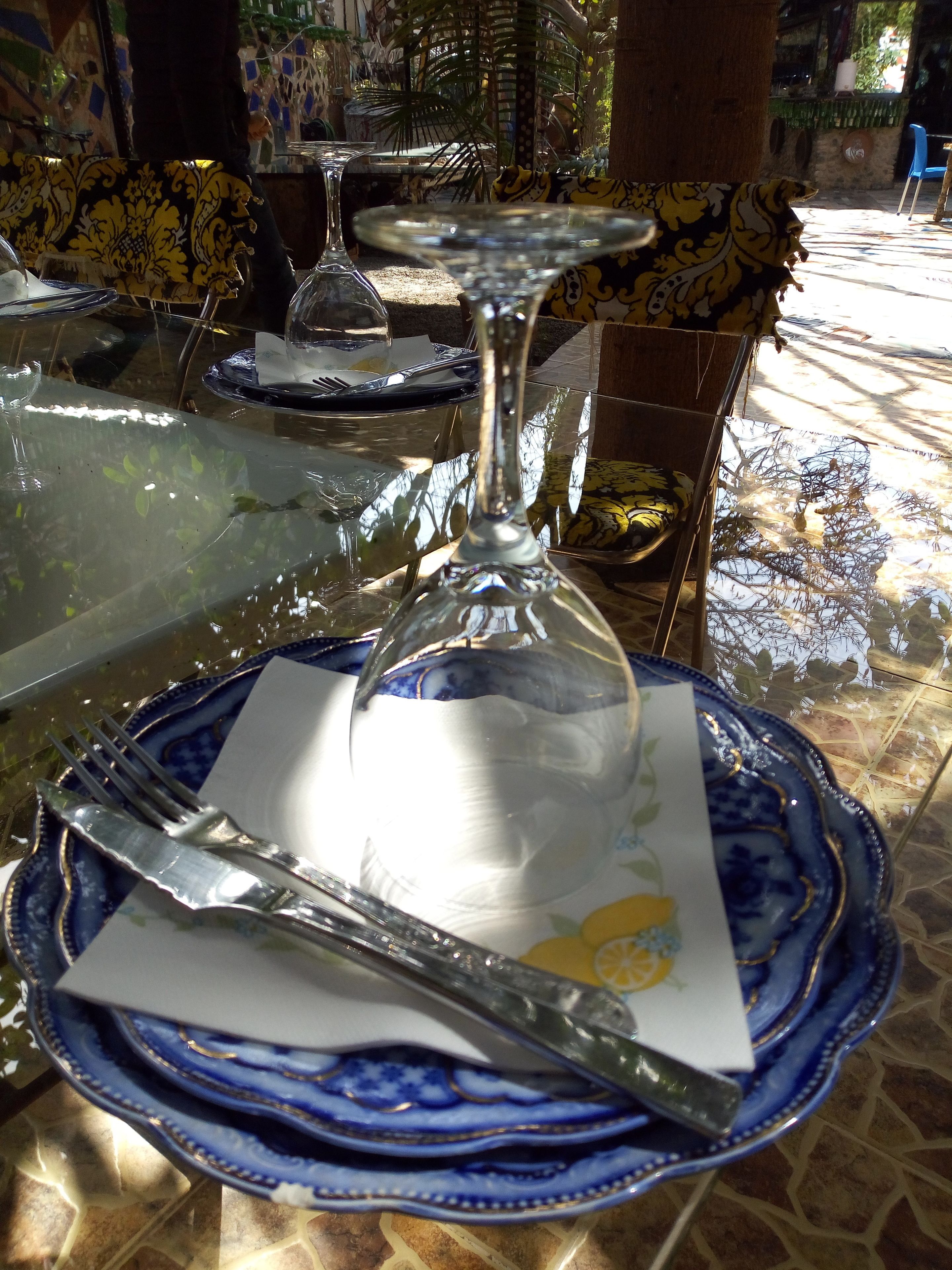 A dining table with a glass top, a blue and white patterned plate, a white napkin, and a silver fork.