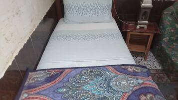A bed with a patterned bedspread, a bedside table with a lamp, and a wall-mounted switch.
