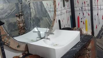 A bathroom with a white sink, a large mirror, and a shower. There are decorative elements on the walls and a towel rack.