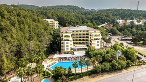 A multi-story hotel with a pool, surrounded by dense forest and hills. - Miarosa Incekum Beach (Alanya)